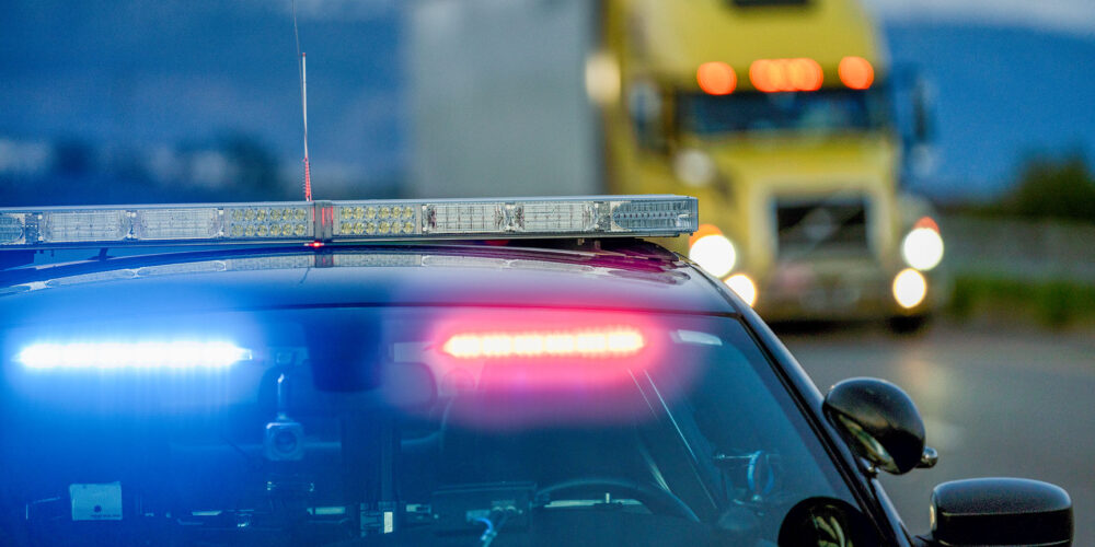 Un patrullero con luces intermitentes se baja del arcén para multar a un conductor mientras pasa un camión.