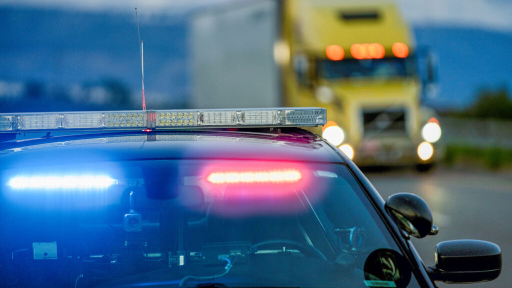 Un patrullero con luces intermitentes se baja del arcén para multar a un conductor mientras pasa un camión.