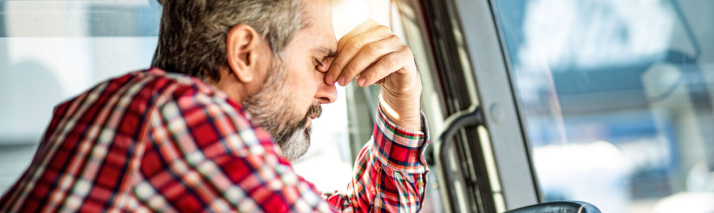 Worried truck driver leaning on a steering wheel and contemplating while waiting in traffic.
