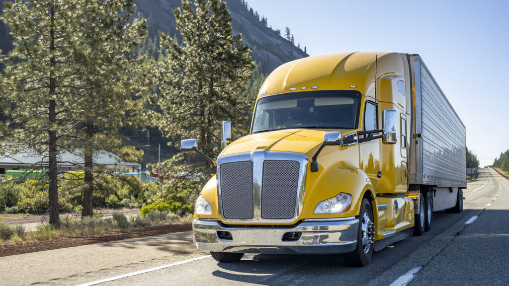 Tracteur semi-remorque jaune classique longue distance avec cabine de chauffeur de camion, compartiment de couchage transportant des marchandises dans une semi-remorque réfrigérée circulant sur la route avec aire de repos sur le côté