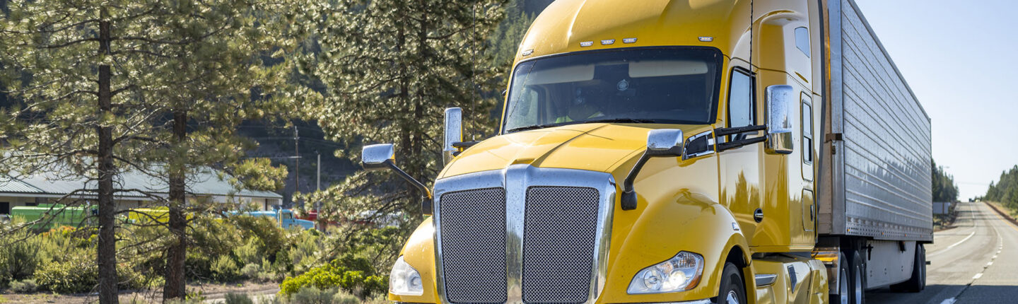Tracteur semi-remorque jaune classique longue distance avec cabine de chauffeur de camion, compartiment de couchage transportant des marchandises dans une semi-remorque réfrigérée circulant sur la route avec aire de repos sur le côté