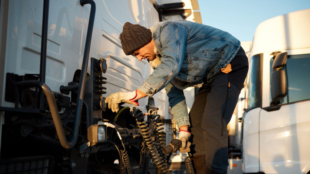 गर्म कपड़े पहने मध्य वयस्क ट्रक चालक ब्रेक एयर होज़ कॉइल की जाँच कर रहा है। पूरी लंबाई का क्लोज़अप