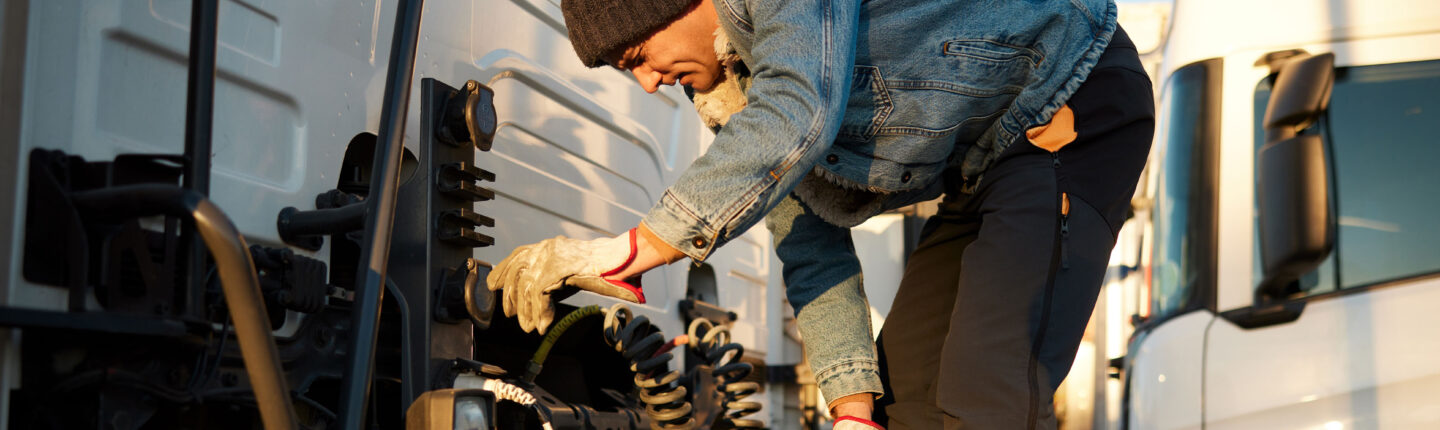Un camionneur adulte d'âge moyen portant des vêtements chauds vérifie la bobine du tuyau d'air de frein. Gros plan sur toute la longueur
